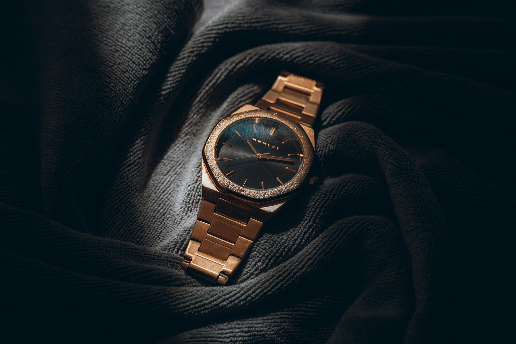 Gold watch resting on dark fabric